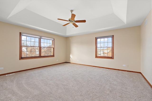 carpeted spare room featuring a healthy amount of sunlight, visible vents, and a tray ceiling