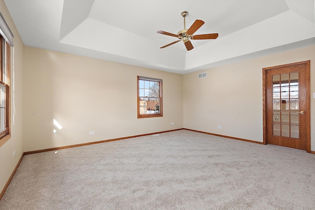 carpeted empty room with a wealth of natural light, a raised ceiling, visible vents, and baseboards