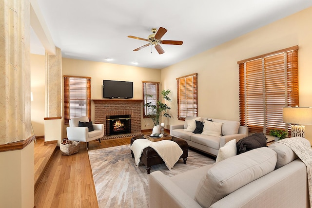 living area featuring a ceiling fan, a brick fireplace, baseboards, and wood finished floors