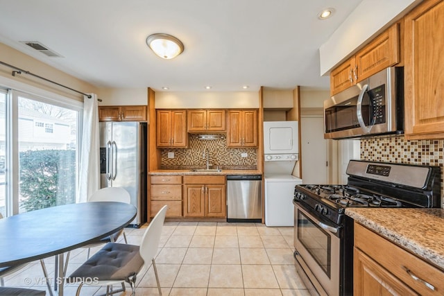 kitchen featuring visible vents, brown cabinets, a sink, stacked washing maching and dryer, and appliances with stainless steel finishes