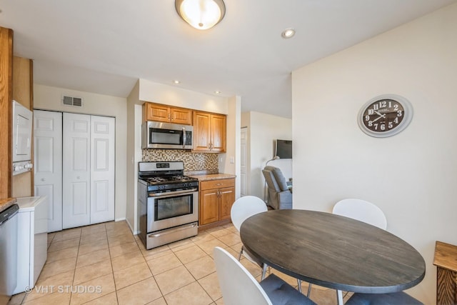 kitchen featuring light countertops, light tile patterned floors, decorative backsplash, stacked washer and clothes dryer, and stainless steel appliances