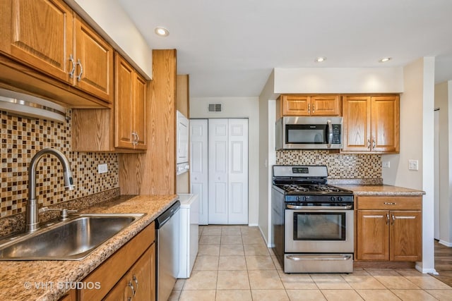 kitchen featuring a sink, stainless steel appliances, brown cabinets, and stacked washing maching and dryer