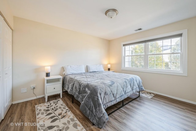 bedroom with a closet, visible vents, baseboards, and wood finished floors