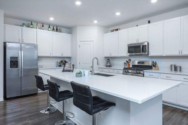 kitchen featuring a breakfast bar area, appliances with stainless steel finishes, dark wood-type flooring, and a sink