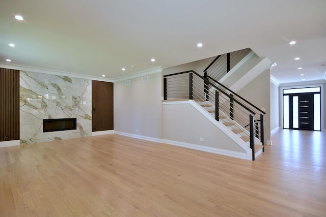 unfurnished living room featuring stairway, ornamental molding, wood finished floors, and a high end fireplace