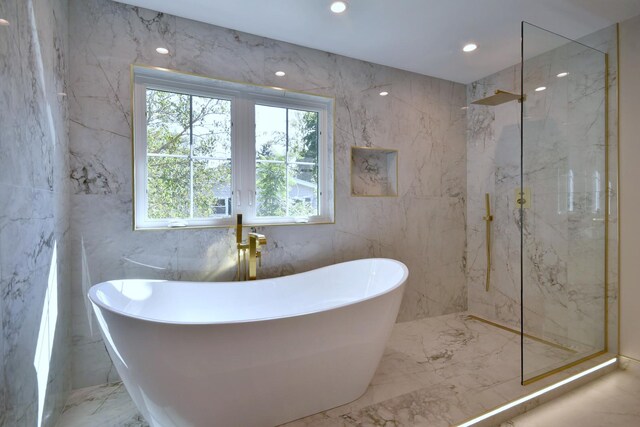 bathroom with marble finish floor, a marble finish shower, stone wall, and a freestanding tub