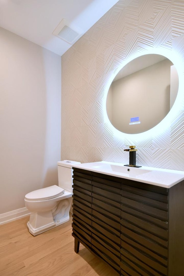 half bath featuring baseboards, visible vents, toilet, wood finished floors, and vanity