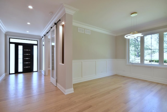 entrance foyer with ornamental molding, a barn door, light wood finished floors, and visible vents