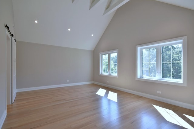 interior space with light wood-type flooring, a barn door, high vaulted ceiling, and baseboards