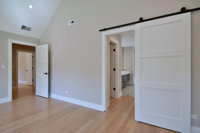 unfurnished bedroom featuring a barn door, light wood-style flooring, visible vents, and baseboards