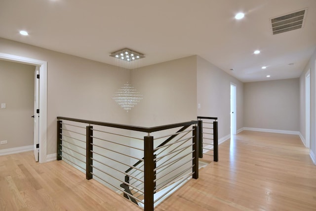 hall with visible vents, light wood-style floors, an upstairs landing, and an inviting chandelier