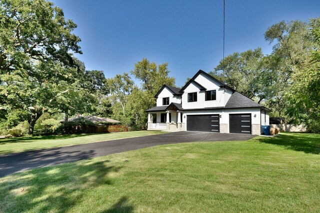 modern farmhouse style home with a shingled roof, a front yard, a garage, stone siding, and driveway