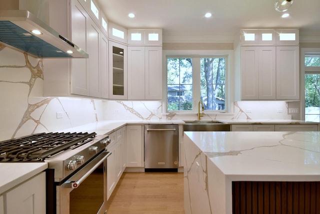 kitchen featuring wall chimney exhaust hood, stainless steel gas range, white cabinetry, and crown molding