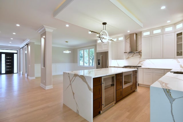 kitchen featuring decorative columns, wall chimney exhaust hood, a kitchen island, wine cooler, and stainless steel appliances