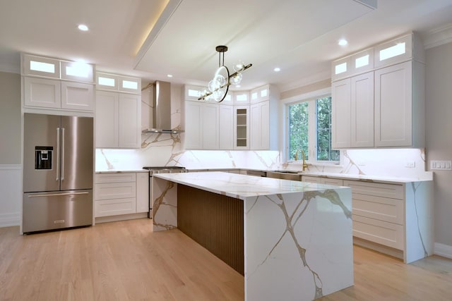 kitchen featuring light wood-style floors, a sink, high quality fridge, and wall chimney exhaust hood