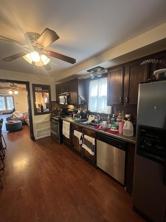 kitchen featuring dark brown cabinetry, decorative backsplash, dark wood-style flooring, stainless steel appliances, and a sink