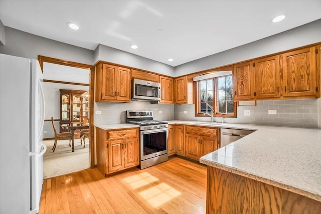 kitchen featuring brown cabinetry, light wood-type flooring, a sink, stainless steel appliances, and tasteful backsplash