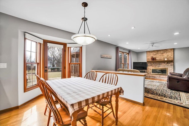 dining area featuring baseboards, recessed lighting, ceiling fan, a brick fireplace, and light wood-type flooring