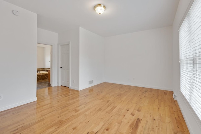 empty room with light wood finished floors, baseboards, and visible vents