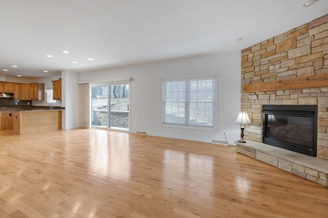 unfurnished living room featuring recessed lighting, visible vents, light wood-style floors, a sink, and a stone fireplace