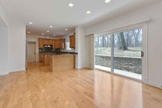 kitchen featuring light wood-style flooring, recessed lighting, under cabinet range hood, freestanding refrigerator, and dark countertops