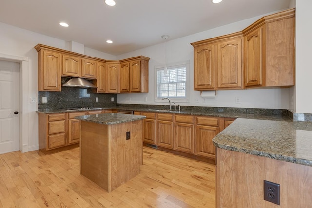 kitchen featuring light wood finished floors, cooktop, a kitchen island, a sink, and under cabinet range hood