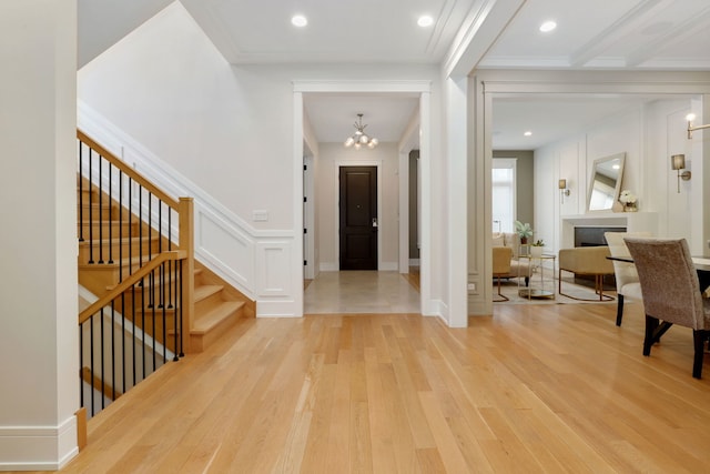 foyer entrance with stairs, a decorative wall, light wood-style flooring, and an inviting chandelier