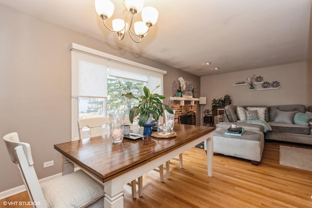 dining space with light wood-style floors, a brick fireplace, baseboards, and an inviting chandelier