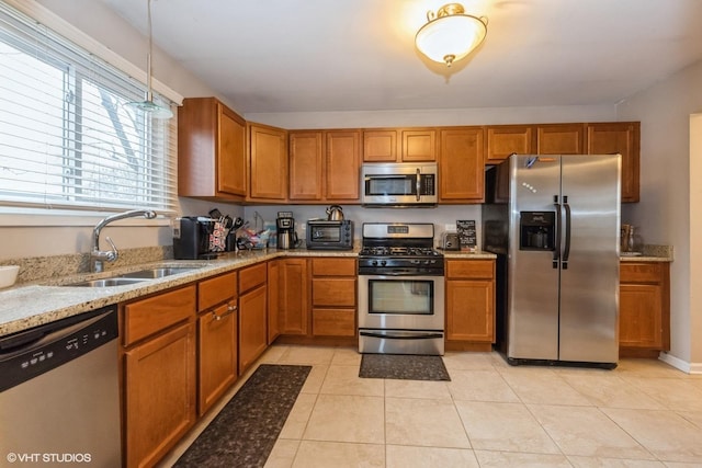 kitchen featuring light stone counters, light tile patterned flooring, stainless steel appliances, a sink, and brown cabinetry