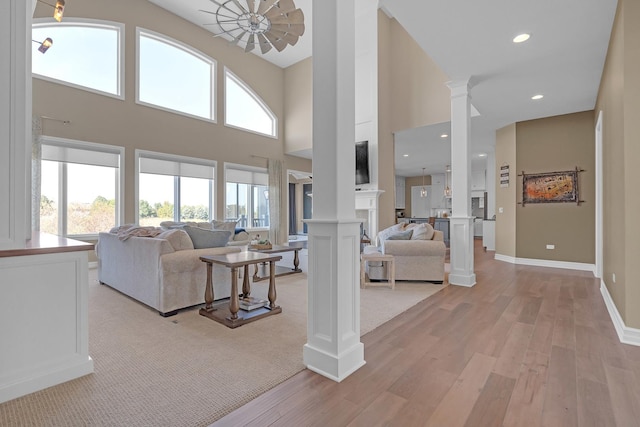 living area with baseboards, light wood-type flooring, a fireplace, and ornate columns