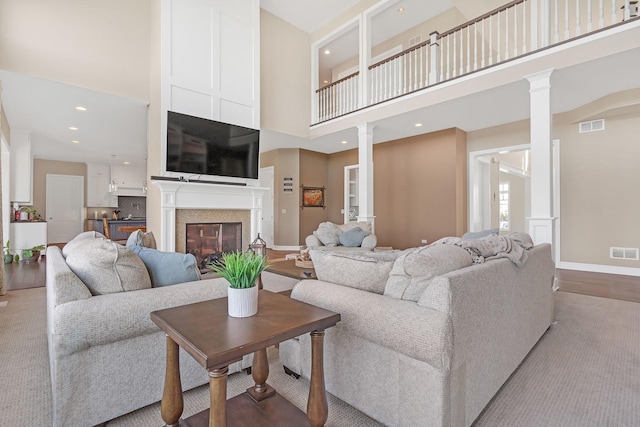 living room with a glass covered fireplace, visible vents, decorative columns, and a towering ceiling