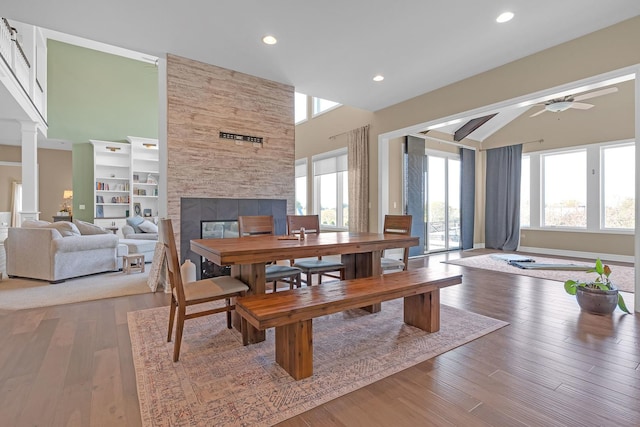 dining area with a ceiling fan, a towering ceiling, ornate columns, light wood-style floors, and a multi sided fireplace