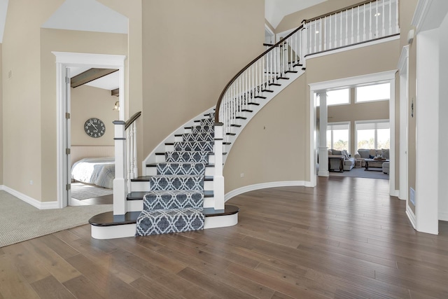 stairs featuring wood finished floors, a towering ceiling, and baseboards