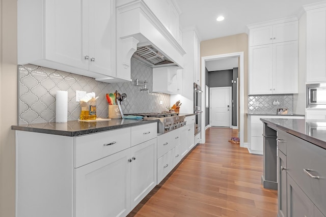 kitchen with stainless steel appliances, tasteful backsplash, custom range hood, light wood-style flooring, and white cabinetry