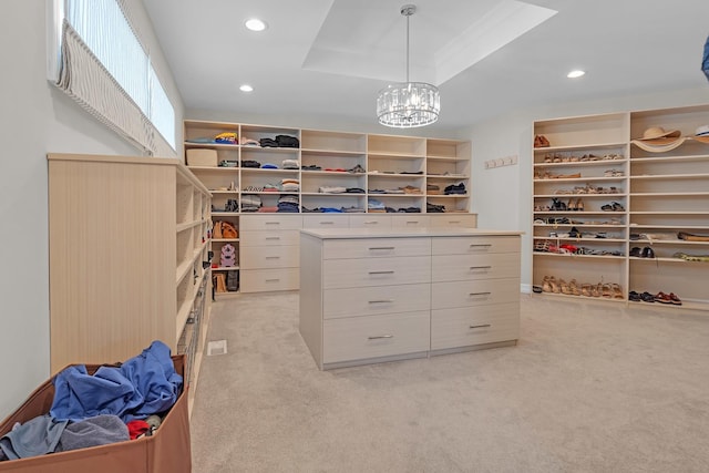 walk in closet with a tray ceiling, a notable chandelier, and light colored carpet