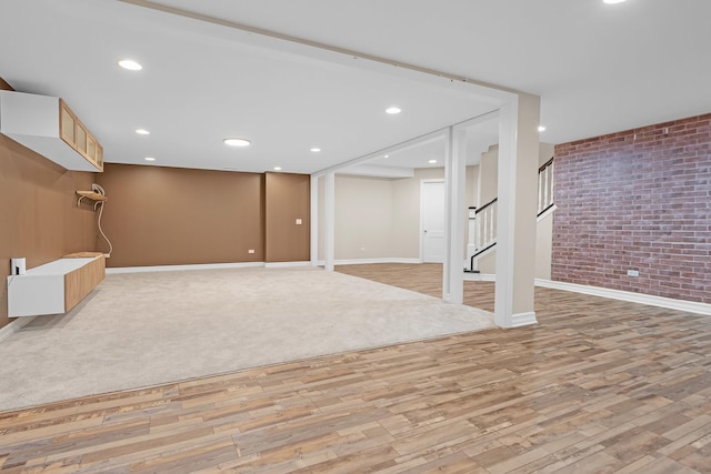 finished basement with baseboards, brick wall, light wood-style flooring, stairway, and recessed lighting