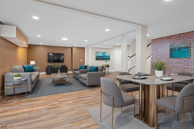 dining area featuring light wood finished floors, recessed lighting, an accent wall, brick wall, and stairs