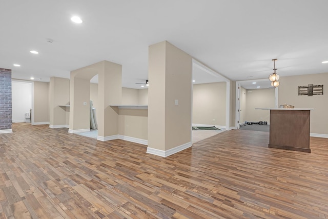 unfurnished living room featuring recessed lighting, baseboards, a bar, and light wood finished floors