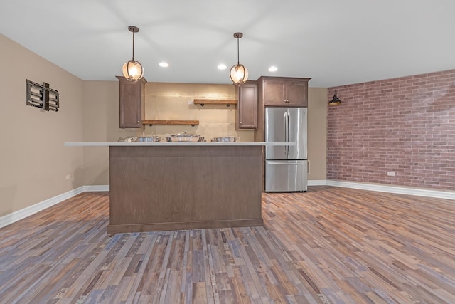 kitchen with brick wall, wood finished floors, freestanding refrigerator, and baseboards