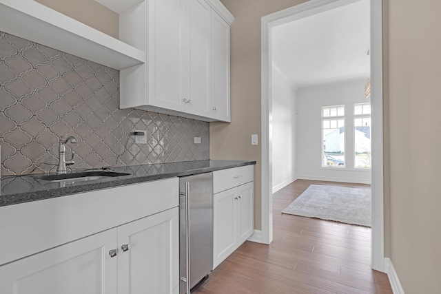 kitchen with a sink, white cabinetry, decorative backsplash, light wood finished floors, and dark countertops