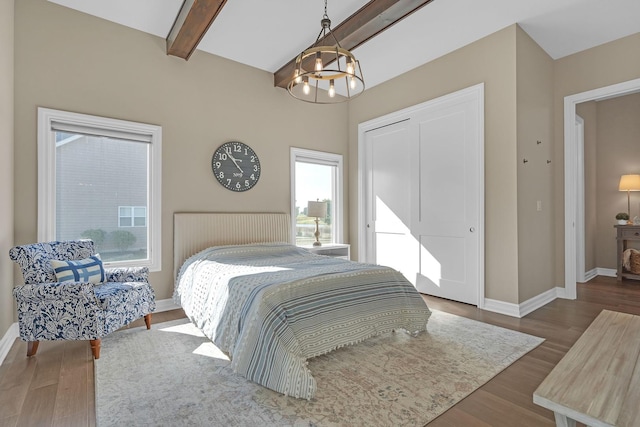 bedroom with a notable chandelier, wood finished floors, baseboards, a closet, and beamed ceiling