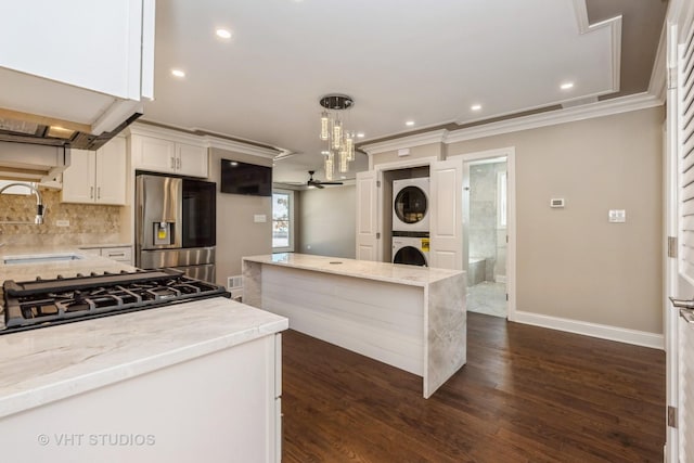 kitchen featuring tasteful backsplash, stacked washer and clothes dryer, stainless steel fridge, white cabinetry, and a sink