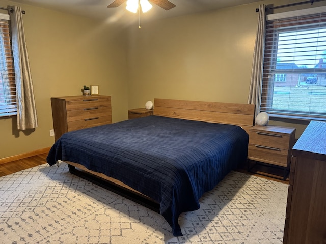 bedroom with light wood-type flooring, a ceiling fan, and baseboards