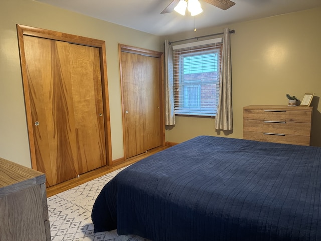 bedroom with a ceiling fan, light wood-style flooring, and two closets