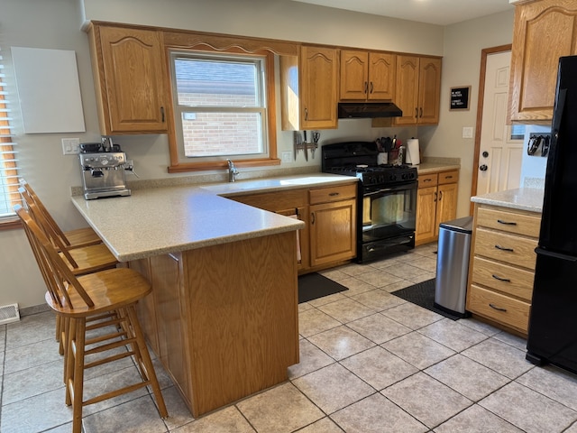 kitchen featuring a peninsula, under cabinet range hood, light countertops, black appliances, and a sink