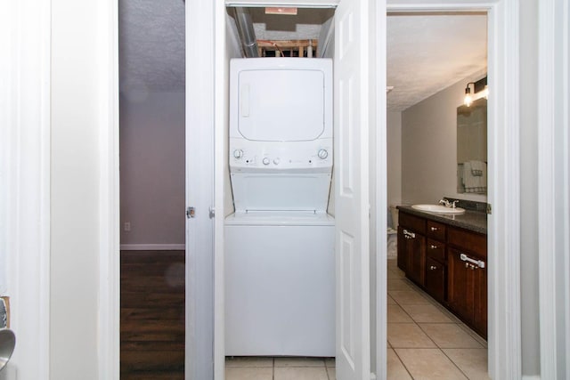 laundry area featuring a sink, light tile patterned flooring, stacked washer / dryer, baseboards, and laundry area