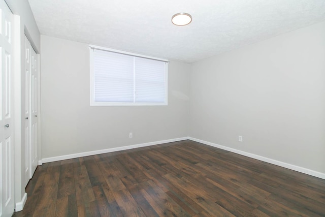 unfurnished bedroom with a closet, baseboards, and dark wood-style flooring