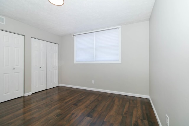 unfurnished bedroom with dark wood-type flooring, baseboards, multiple closets, and visible vents