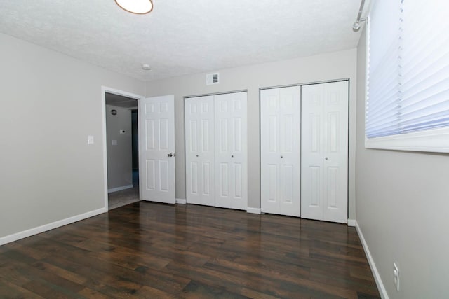 unfurnished bedroom featuring visible vents, two closets, baseboards, wood finished floors, and a textured ceiling