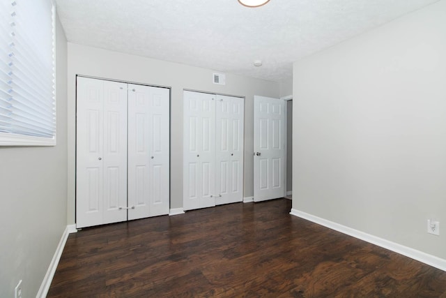 unfurnished bedroom with two closets, dark wood-type flooring, and baseboards